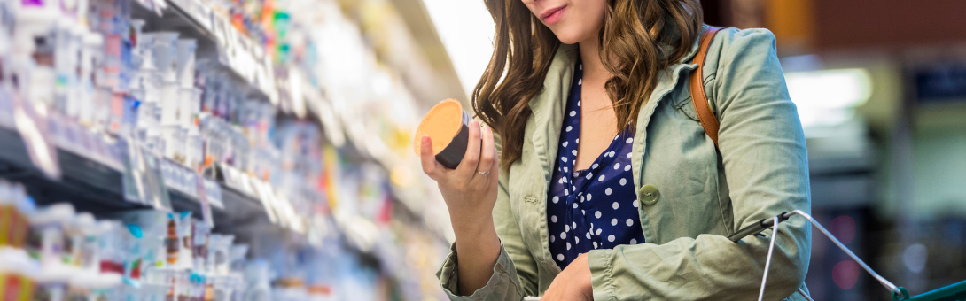 Vrouw met groene jas en blauwe bloes die het etiket van een yoghurt leest