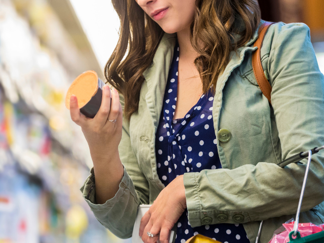 Vrouw met groene jas en blauwe bloes die het etiket van een yoghurt leest